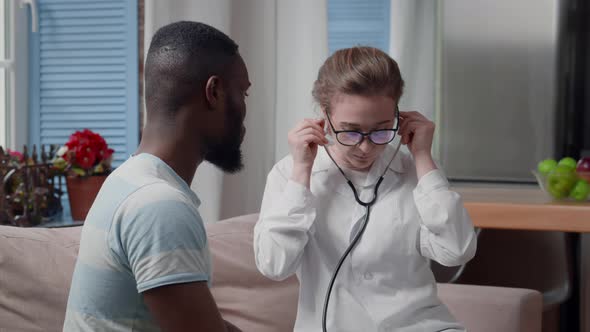 Woman Doctor Examine Sick AfricanAmerican Ethnicity Patient with Stethoscope at Home alt