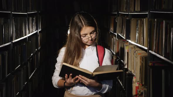 Girl with Glasses Reading a Book in the Library alt