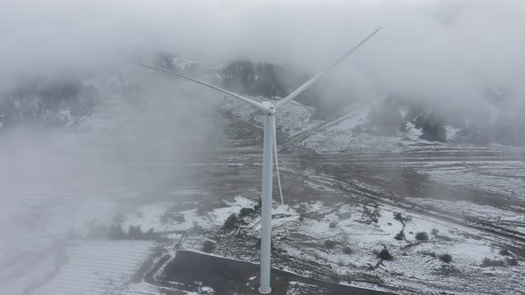 Wind turbine in a snowy landscape with early winter morning mist. alt