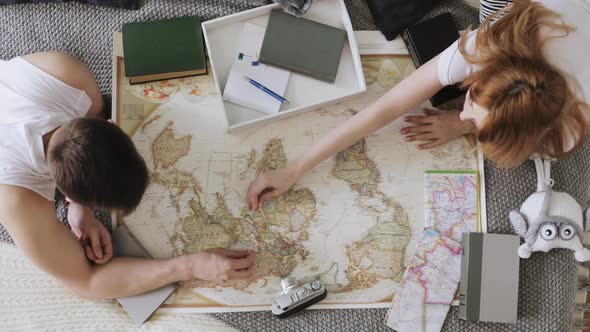 Man and Woman Are Planning Vacation Using a World Map and Other Travel Accessories. alt