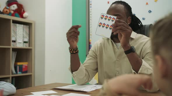 African American Teacher Teaches Teenagers Showing Cards Sitting at the Desk in the Classroom alt
