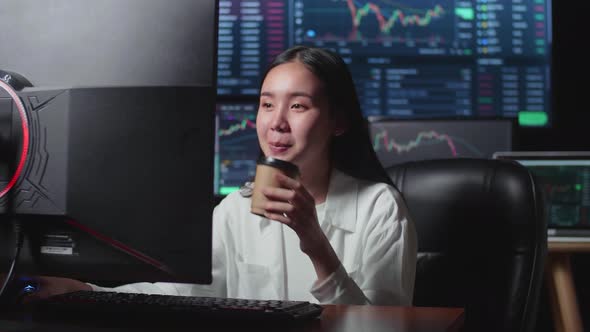 Asian Female Stock Market Broker Drinking Coffee And Working On Computer alt