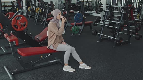 Muslim Woman Sitting in Gym and Drinking Water alt