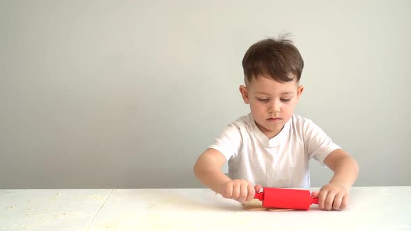 Child Hands Rolling Dough with a Rolling Pin. Boy Rolls Out the Dough on the Kitchen Table