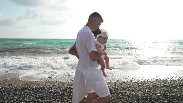 Side View of Caucasian Man Asian Woman and Baby Girl Strolling on Sunny Mediterranean Sea Coast with alt