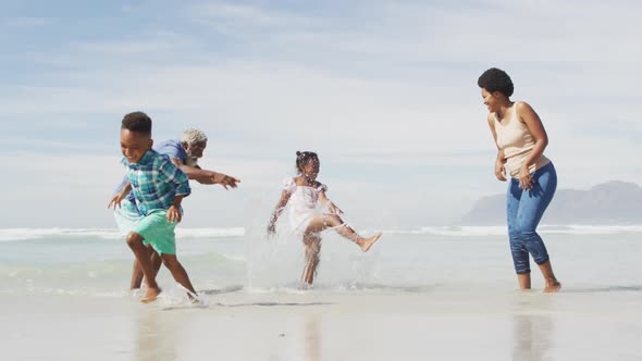 Happy african american couple playing with children on sunny beach alt