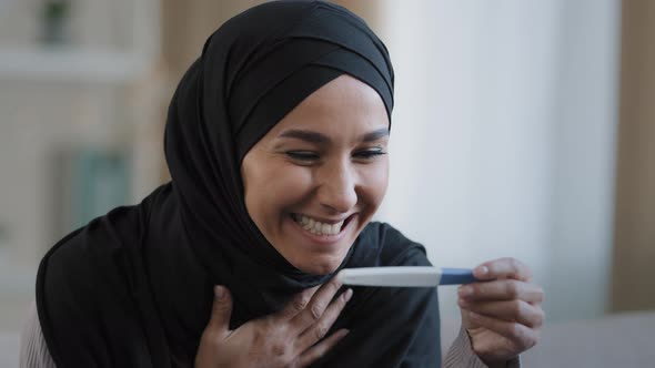 Joyful Islamic Young Woman in Hijab Smiling Happily Holding Pregnancy Test Excited Pregnant Lady alt