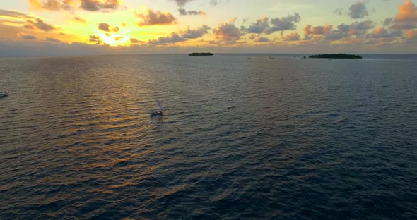 Aerial drone view of a man and woman sailing on a boat to a tropical island at sunset. alt