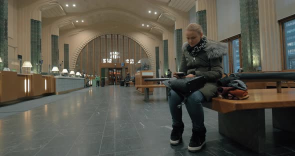 Woman waiting in station hall and using smart phone alt