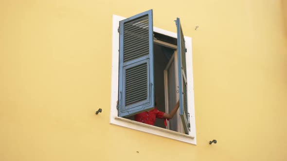 A woman opens shutters on a window traveling in a luxury resort town in Italy, Europe alt