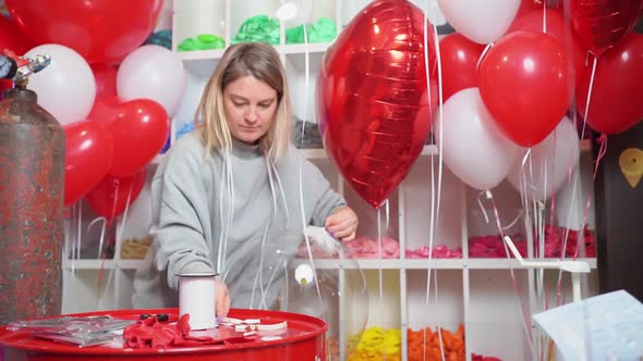 Woman Ties with a Ribbon a Round Transparent Balloon with White Feathers Inside alt