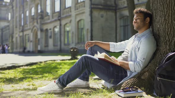 Mixed-Race Guy Sitting Under Tree, Waving and Smiling at Somebody, Friendly alt