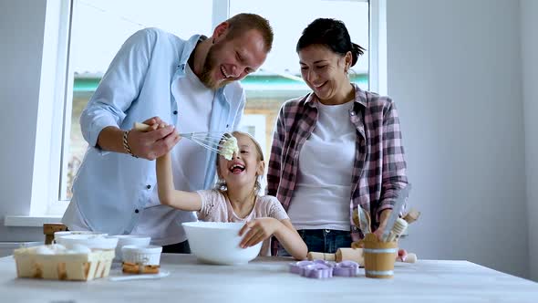 Mother, father and daughter preparing dough together in kitchen, alt