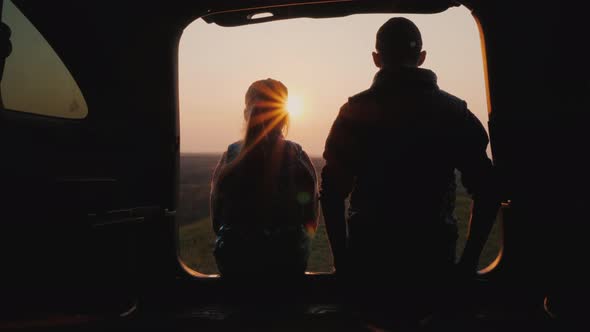 Teenager with Younger Sister Sitting in the Trunk of a Car, Watching the Sunset alt