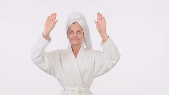 A beautiful adult elderly woman wearing a bathrobe and towel over her head showing hands alt