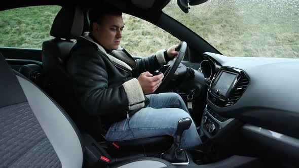 The Driver of the Car is Sitting in the Car and Looking at the Phone