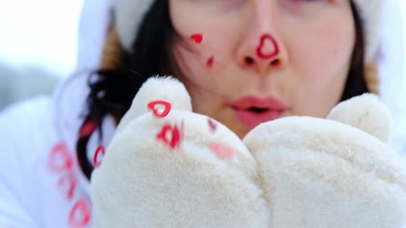 A woman blows red sequins in the shape of hearts from warm fur mittens alt