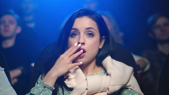 Shocked Woman Watching Scary Moment in Cinema. Scared Girl Licking Lips Indoor. alt