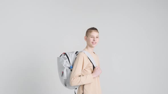 Happy boy teenager in beige clothes with gray backpack behind his back smiles at the camera