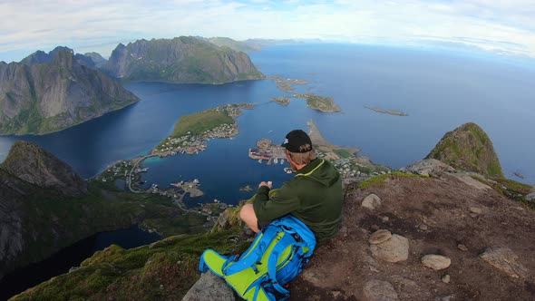 Traveler man sitting on a hill of beautiful norway fjord Reinebringen near Reine town, Lofoten Islan alt