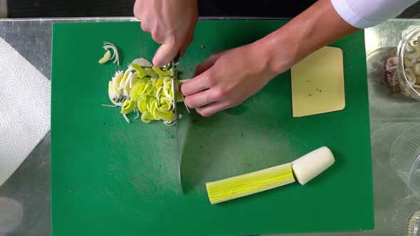 Slicing porreya with a steel knife on a green background