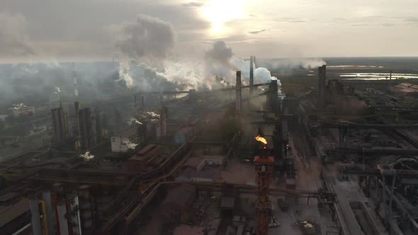 Steel Factory Pipes During Sunrise Time. High Above Metallurgical Plant and Smoke Cloud Is Coming alt