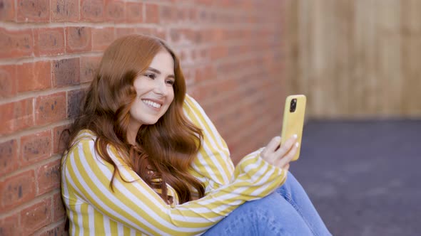 Smiling woman sitting in backyard having video call on smartphone