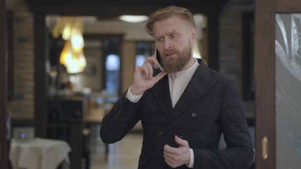 Portrait of a Successful Business Man with a Red Beard Talking on His Cell in an Expensive alt