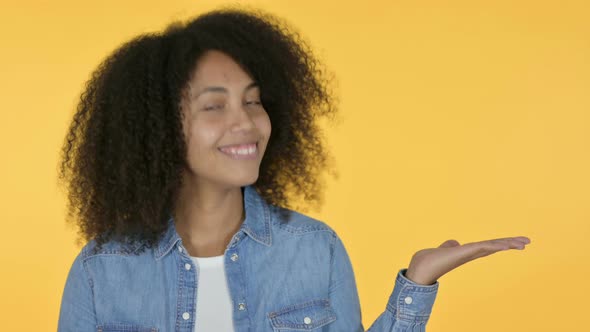 African Woman Holding Product on Palm, Yellow Background  alt