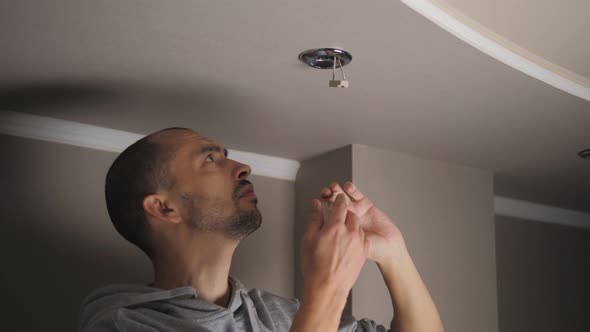 Young Man Repairing Cable Wiring and Installs or Replaces the Halogen Lamp on the Ceiling alt