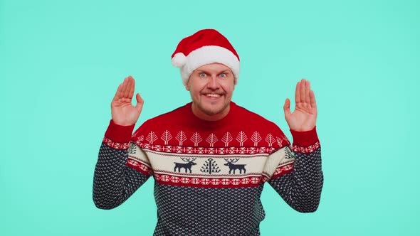 Man in Sweater Santa Christmas Hat Fooling Around Having Closing Eyes with Hand and Spying Through alt