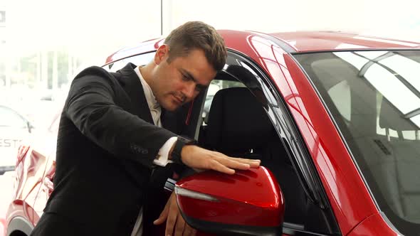 A Cheerful Salesman Points To the Excellent Quality of the Car