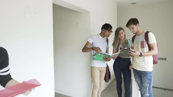 Students reading book and using digital tablet in college corridor alt