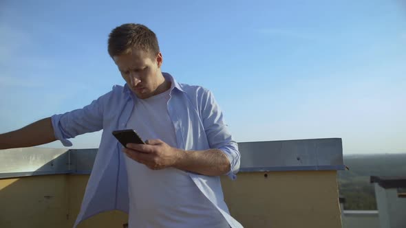 Dissatisfied Young Man With Cocktail Chatting Smartphone on Balcony, Problems