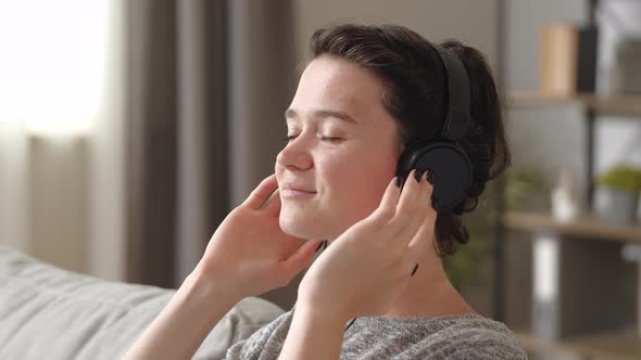 Close Up View Tranquil Beautiful Woman Lean on Comfy Couch Wear Wireless Headphones Closing Eyes alt