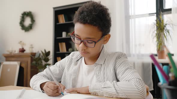 Zoom Out Portrait of Clever Concentrated African American Boy Wearing Eyeglasses Learning at Home alt