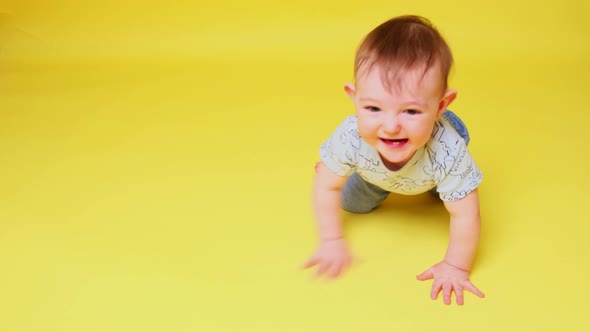 Happy toddler baby boy crawls on studio yellow background. Smiling baby crawling fast on the floor,