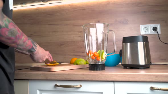 Tattooed Male Hands Cutting Orange on the Counter for Morning Smoothie alt