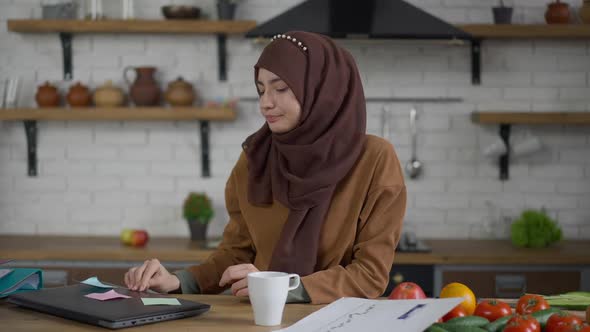 Young Female Middle Eastern Startuper Closing Laptop and Thinking Sitting in Kitchen alt