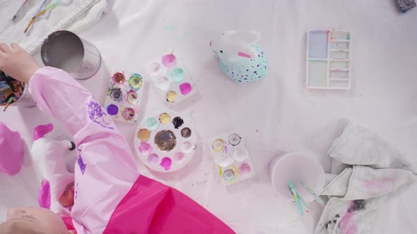 Flat lay. Little girl painting paper mache figurines with acrylic paint  for her homeschooling art p alt