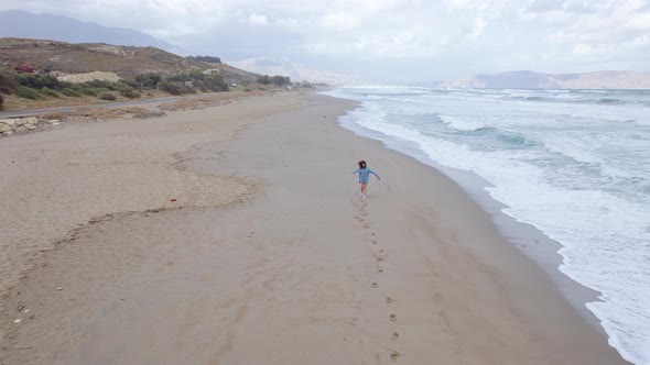 Drone footage of a woman running along the ocean coastline and leaving footprints in the sand. alt