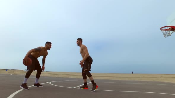 A man takes a jump shot while playing one-on-one basketball hoops on a beach court alt