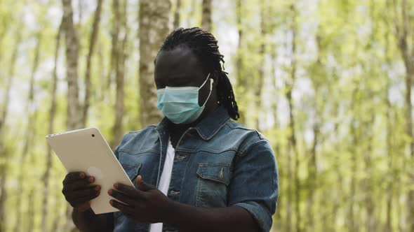 An African Man with Medical Mask Using the Tablet in the Forest. Wireless or Future Technology alt
