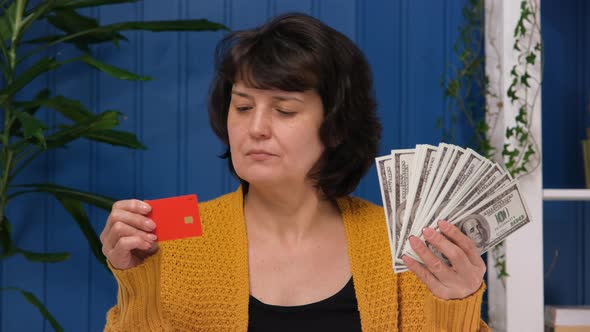 Middle Aged Woman is Holding Credit Card and Money and Choose Cash Money Dollar alt