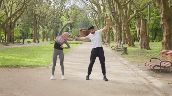 Active Woman in Sport Clothes and Hijab Stretching Legs at Summer Park alt
