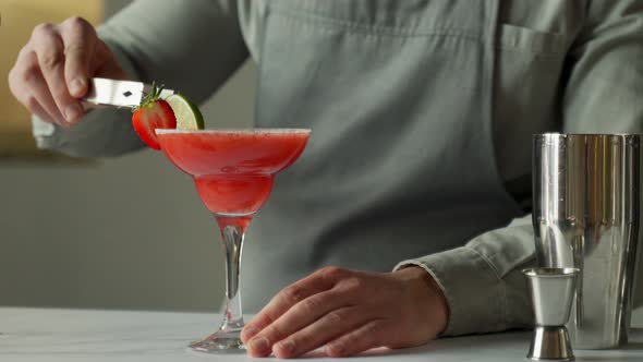 Man Bartender Prepares a Margarita Cocktail Decorates the Glass with Lime and Strawberries alt