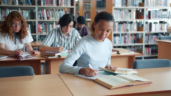 Slow Motion of Pretty Mixed Race Girl Studying in Library with Group of People alt