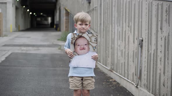 Slow motion push of young boy holding up baby photo of himself with cleft palate. alt