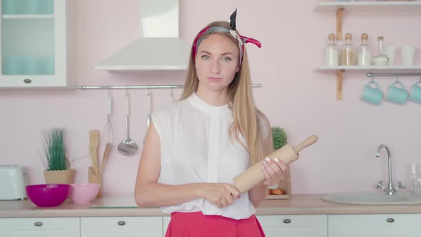 Young Angry Woman Holding Rolling Pin and Looking at Camera. Portrait of Dissatisfied Housewife with alt