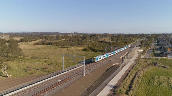 Aerial chase shot following train as it arrive at elevated station over skatepark beneath alt